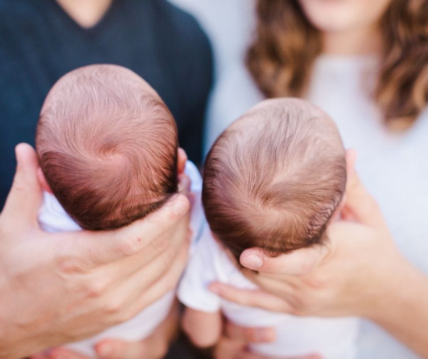 Top-down view of a man and woman holding the heads of twin newborn babies.