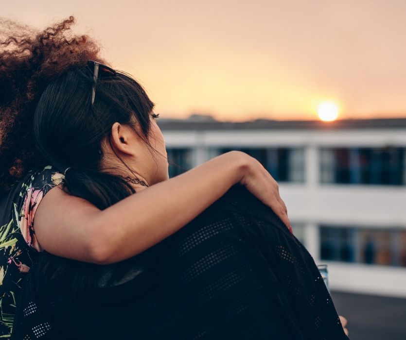 Two friends embracing and looking out at a sunset over the city from a rooftop.