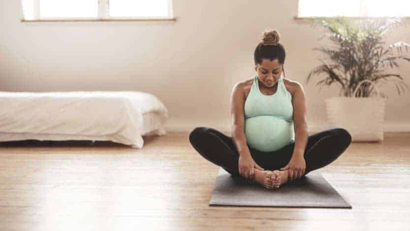 Pregnant woman sitting on a yoga mat in a butterfly stretch at home.